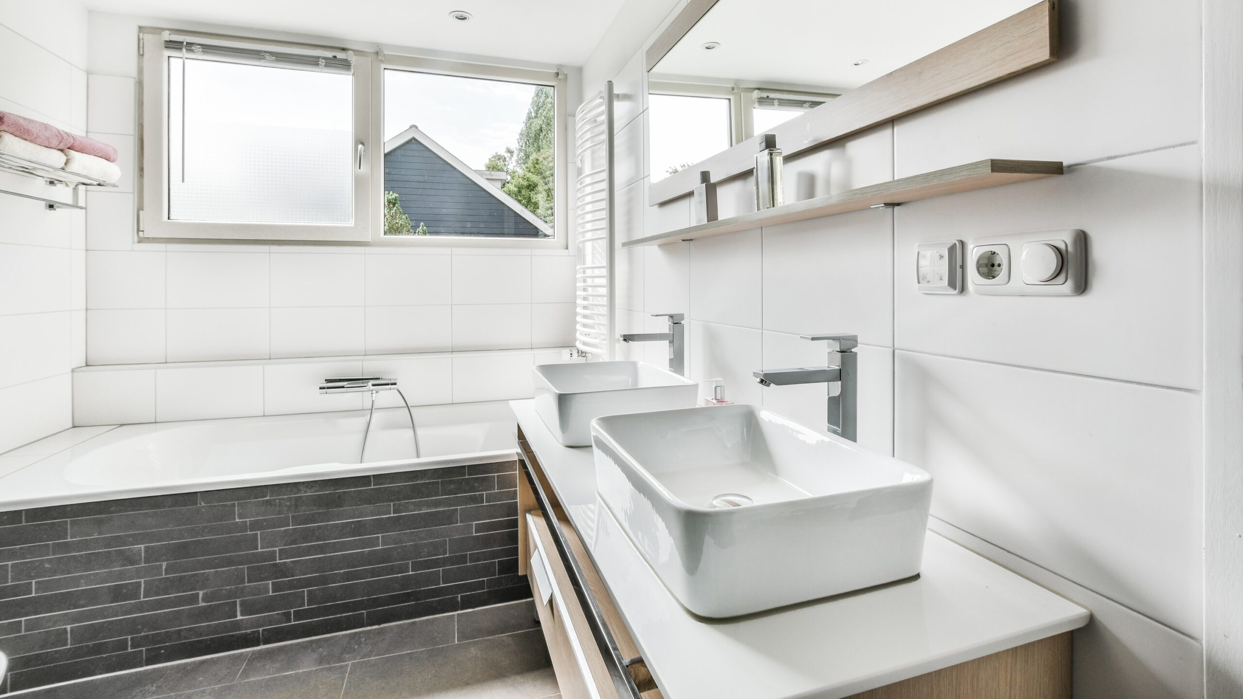 Bathroom with white exterior, white-framed windows, white sink, and bathtub with dark grey brick themed foundation