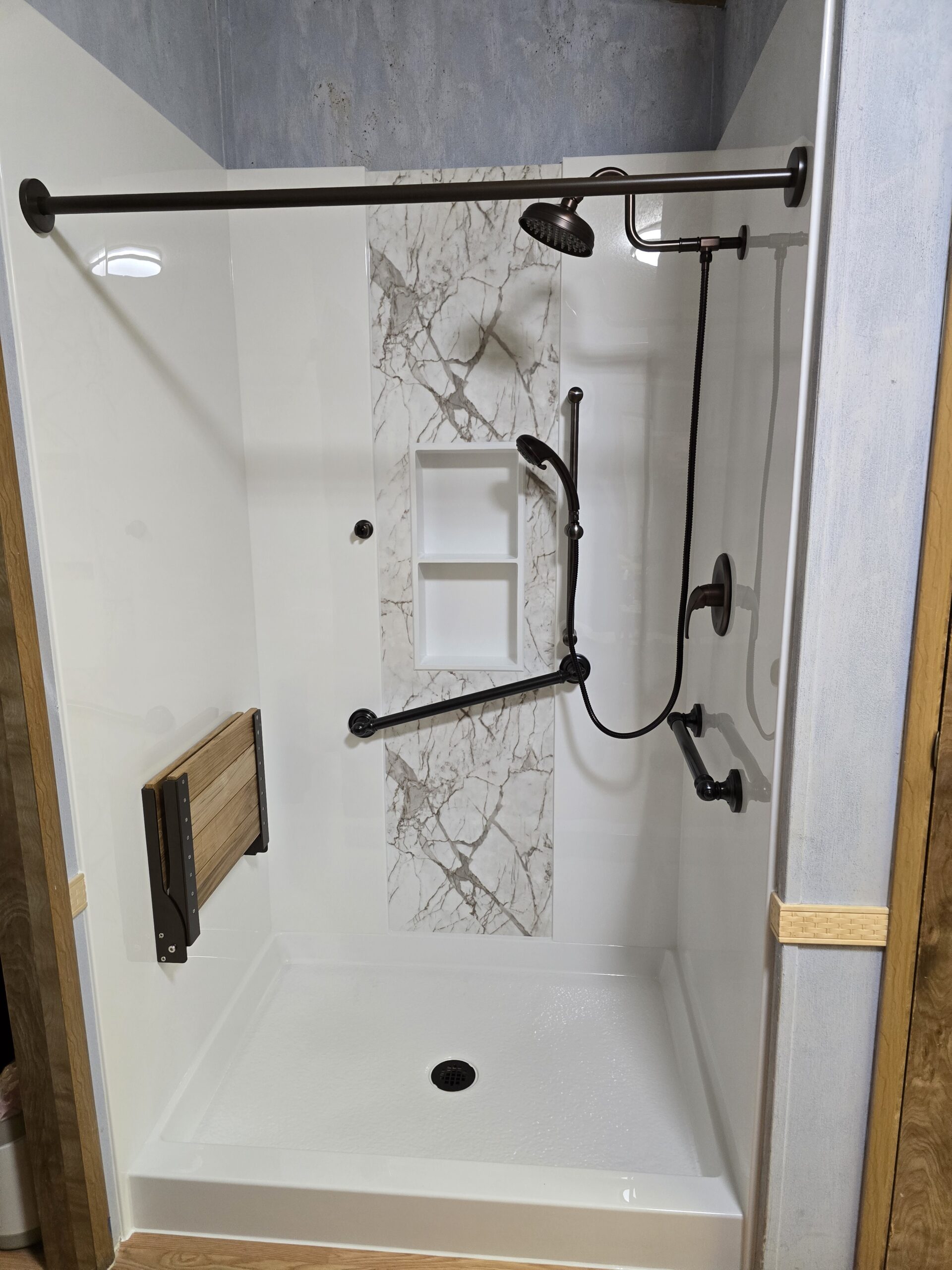 White walk-in shower with a flip-up seat, handrails, and black features