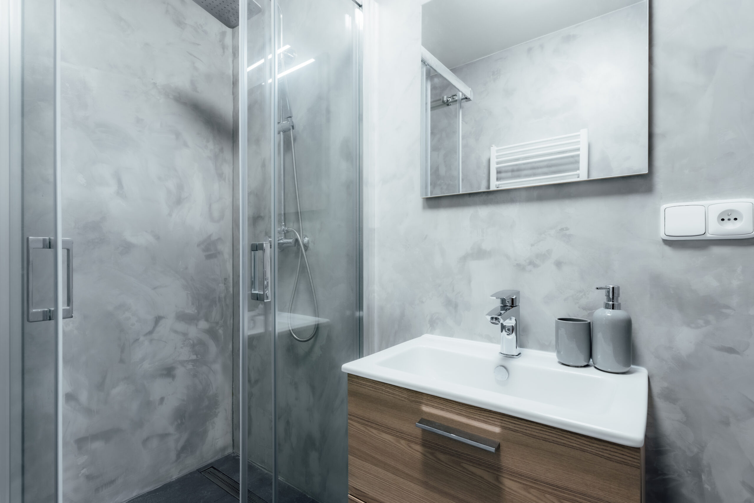 Close-up of a walk-in shower with modern fixtures and gray backsplash